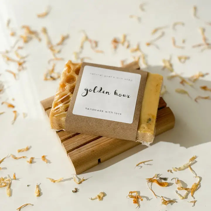 Bar of soap with a 'golden hour' label on a wooden block, surrounded by dried flowers.