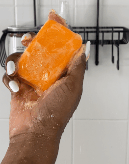 Passion Fruit Soap held in hand under water with a shower rack in the background.
