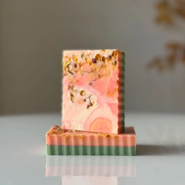 Marbled soap bar with pink, green, and gold colors on a reflective surface.