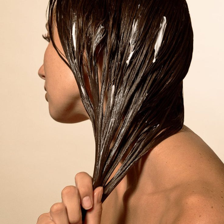 Person with wet hair holding it back against a beige background