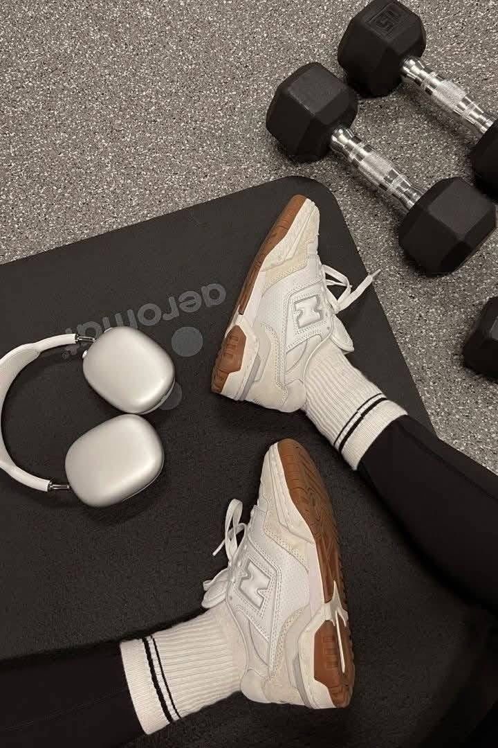 White sneakers with brown soles on a black mat with dumbbells and earphones.