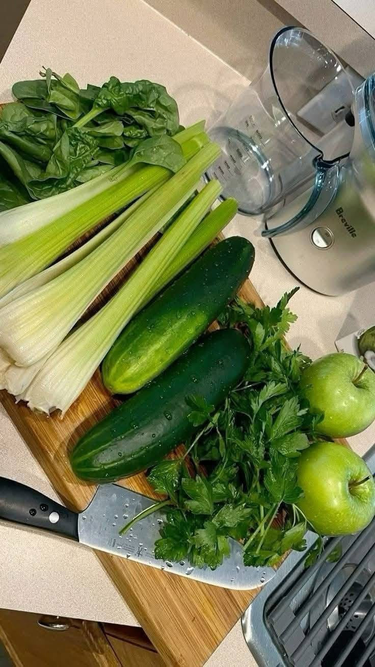 Vegetables including celery, cucumbers, and apples on a cutting board with a knife.