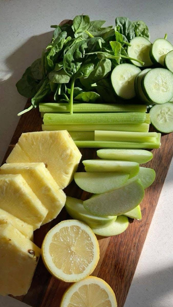 Sliced pineapple, lemons, cucumbers, and celery on a wooden cutting board.