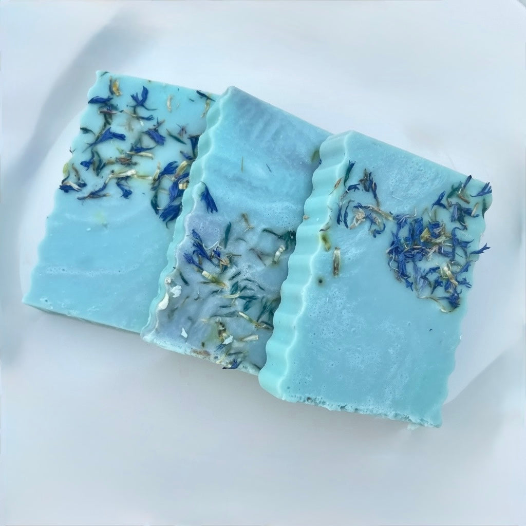 Three pieces of blue soap with floral embedded design on a white plate
