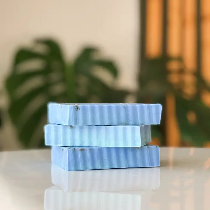 Stack of blue striped soap bars on a reflective surface with a blurred plant background